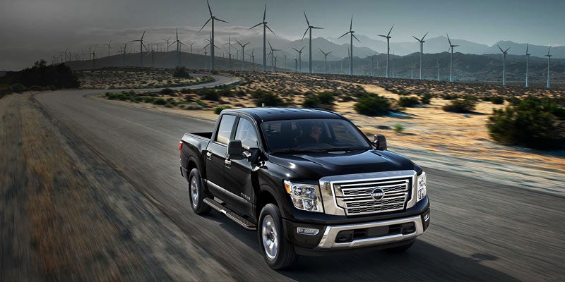 Black Nissan Titan truck driving near wind turbines on a desert road