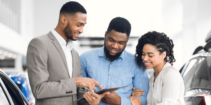 Car salesman shows tablet to smiling couple at dealership