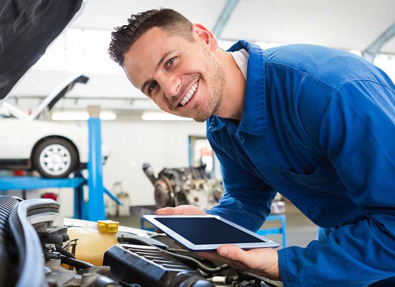Smiling auto technician using a tablet while working in a car repair shop